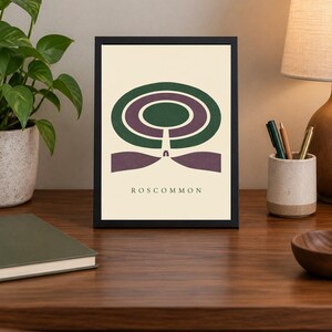 May include: A framed rectangular art print featuring a graphic illustration of a green and purple circular maze design on a cream background. The word ROSCOMMON is printed in black capital letters at the bottom centre of the artwork.