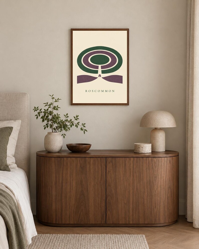 May include: A framed wall art print featuring a graphic design with concentric green and purple oval shapes above a purple base, with the text ROSCOMMON printed in black at the bottom, all set against a cream-coloured background.