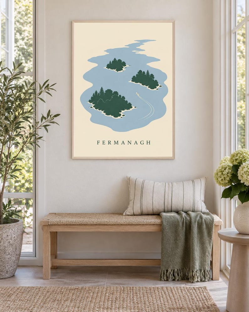 May include: A rectangular wall art print featuring a light blue lake with three dark green islands covered in trees. A small white boat leaves a wake on the water. The background is cream-colored, and the word FERMANAGH is printed in black.