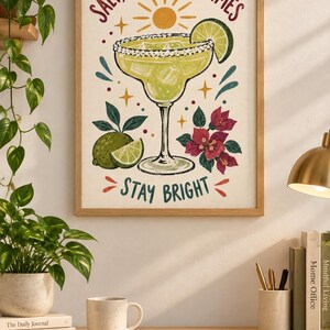 May include: A framed wall art print featuring a margarita in a glass with a lime wedge, ice cubes, and salt rim. The text reads SALT, CITRUS, GOOD TIMES and STAY BRIGHT. The illustration includes a yellow sun, green limes, and pink flowers.