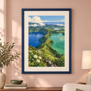 Puede incluir: Una impresi&oacute;n de paisaje enmarcada que muestra una vista elevada de dos lagos de cr&aacute;ter volc&aacute;nico adyacentes, uno azul profundo y otro turquesa, separados por una cresta verde. Flores de hortensia blancas florecen en primer plano bajo un cielo azul.