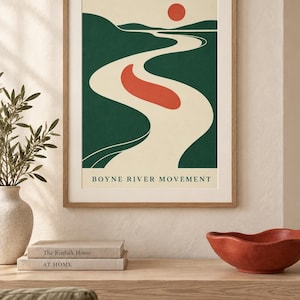 May include: A framed wall art print titled BOYNE RIVER MOVEMENT featuring a stylized landscape with a winding cream-colored river, dark green hills, a solid red sun, and a red abstract shape floating in the center of the river against a cream background.