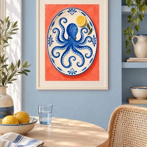 May include: A framed wall art print featuring an oval white platter with a blue octopus illustration and a yellow lemon slice, set against a vibrant orange background. The artwork is displayed in a light-coloured wooden frame on a blue wall.