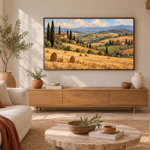 May include: A rectangular wall art print featuring a landscape of a golden wheat field with hay bales, cypress trees, and stone buildings under a blue sky, displayed in a thin dark frame mounted on a light-colored wall above a wooden console.