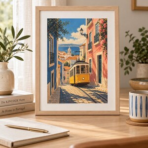 K&ouml;nnte beinhalten: Ein gerahmter Kunstdruck zeigt eine gelbe Stra&szlig;enbahn, die eine gepflasterte Stra&szlig;e entlangf&auml;hrt, ges&auml;umt von blauen und rosafarbenen Geb&auml;uden, unter einem klaren blauen Himmel mit Blick auf das Meer.