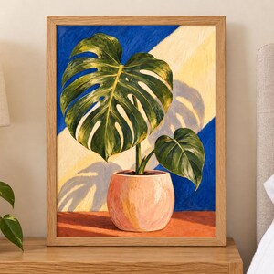 Puede incluir: Un cuadro enmarcado de una planta monstera verde en una maceta color melocot&oacute;n. El fondo presenta rayas diagonales azules y amarillas, con una sombra oscura proyectada sobre la superficie. La obra est&aacute; en un marco de madera clara.