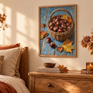 May include: A framed wall art print featuring a woven basket filled with brown chestnuts resting on a weathered blue wooden surface, accompanied by scattered autumn leaves in shades of orange and yellow, capturing a seasonal harvest theme.