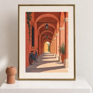 Pu&ograve; includere: Una stampa artistica incorniciata che raffigura un porticato color terracotta con una bicicletta blu appoggiata a un pilastro. La scena presenta lanterne sospese, una pianta in vaso e piante rampicanti, il tutto in una cornice dorata.
