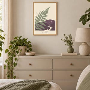 May include: A rectangular wall art print in a light wood frame featuring a green fern frond overlapping a purple mountain landscape with a winding river and the text LAOIS printed in black at the bottom centre of the cream-coloured background.