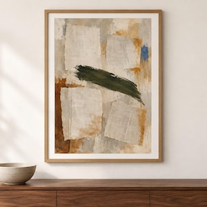 May include: A framed abstract wall art print featuring a collage-style composition of torn paper shapes in shades of beige and cream, layered over textured brown and grey washes, with a prominent dark green brushstroke and a small blue accent.