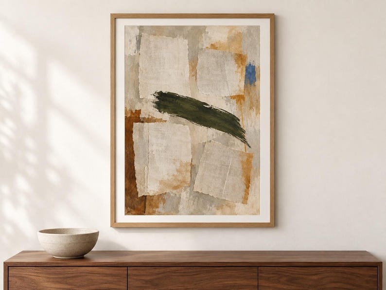May include: A framed abstract wall art print featuring a collage-style composition of torn paper shapes in shades of beige and cream, layered over textured brown and grey washes, with a prominent dark green brushstroke and a small blue accent.