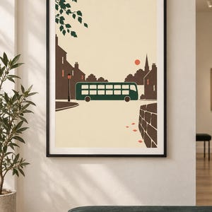 May include: A framed wall art print featuring a stylized illustration of a dark green double-decker bus driving through a town street. The scene includes brown silhouettes of buildings, a street lamp, a small red sun, and green tree leaves.