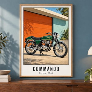 May include: A framed wall art print featuring a green Norton Commando motorcycle parked in front of an orange garage door. The text at the bottom reads COMMANDO Norton 1968 in black capital letters against a white background within the print.