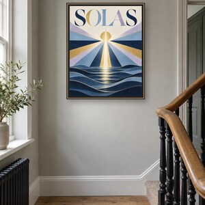 May include: A framed rectangular wall art print featuring the word SOLAS in bold dark blue letters at the top. Below the text, a stylized sun emits golden and blue rays over dark blue ocean waves, creating a geometric sunrise scene.