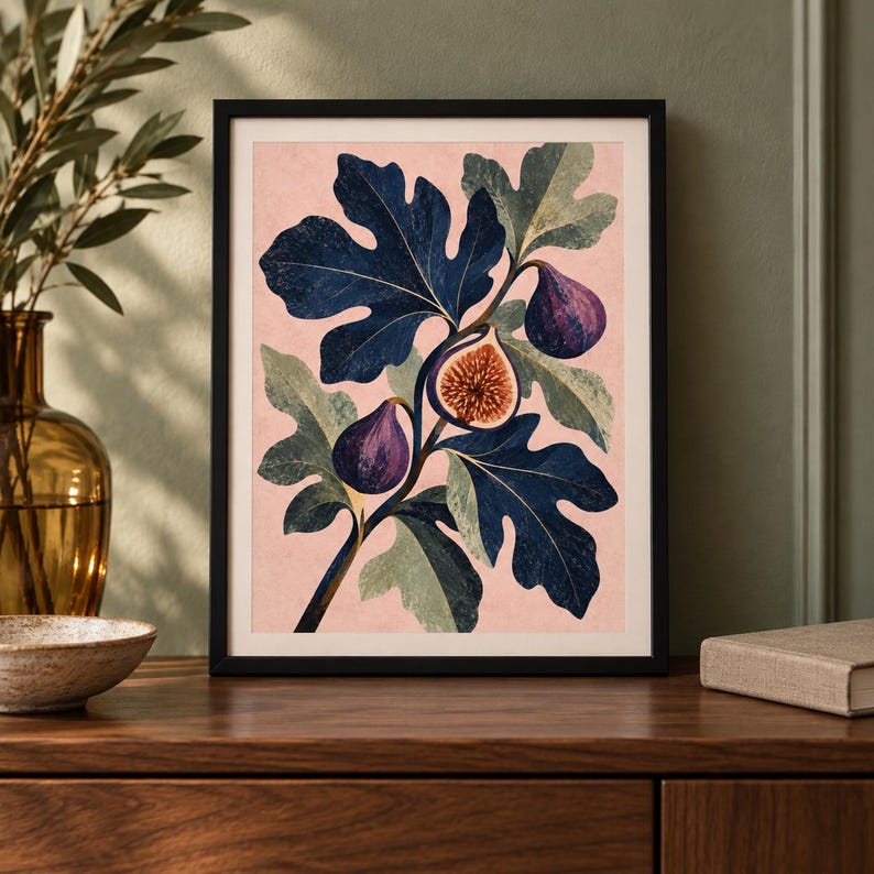 May include: A framed wall art print featuring a botanical illustration of a fig branch with dark blue leaves and purple figs against a light pink background. One fig is sliced open to reveal a textured, golden-brown interior with visible seeds.