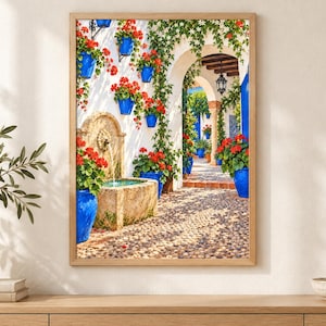 May include: A framed wall art print depicting a Mediterranean courtyard scene with a stone fountain, vibrant red geraniums in bright blue pots, climbing green vines on white walls, and a cobblestone path leading through a stone archway.