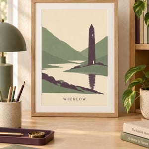 Peut inclure: Une impression d'art encadr&eacute;e pr&eacute;sentant une illustration paysag&egrave;re stylis&eacute;e d'une haute tour violet fonc&eacute; situ&eacute;e pr&egrave;s d'une rivi&egrave;re et de collines vertes, avec le texte WICKLOW imprim&eacute; en noir au centre inf&eacute;rieur du fond cr&egrave;me.