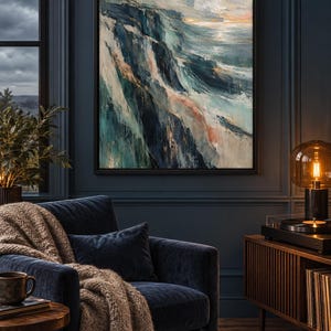 Op de afbeelding: Een rechthoekig ingelijst kunstwerk aan de muur met een abstract landschapsschilderij met dikke, getextureerde penseelstreken in tinten diep marineblauw, taling, wit en zacht perzik, dat een ruige kustlijn bij een woelige oceaan toont.