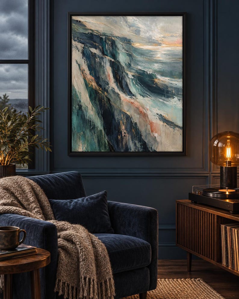 Op de afbeelding: Een rechthoekig ingelijst kunstwerk aan de muur met een abstract landschapsschilderij met dikke, getextureerde penseelstreken in tinten diep marineblauw, taling, wit en zacht perzik, dat een ruige kustlijn bij een woelige oceaan toont.