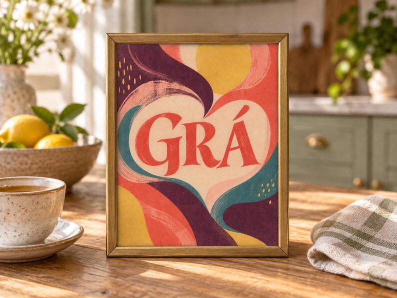 May include: A rectangular framed print featuring the word GR&Aacute; in bold red letters centred within a cream-coloured heart shape. The background consists of abstract, flowing shapes in shades of yellow, red, dark purple, and teal with small yellow dashes.