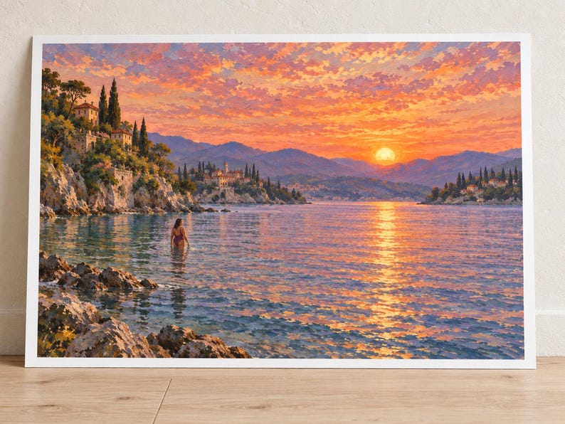 May include: A rectangular art print featuring a coastal landscape at sunset. The scene depicts a calm sea with a person wading in the water, rocky cliffs with Mediterranean-style buildings, distant mountains, and a vibrant orange and pink sky.
