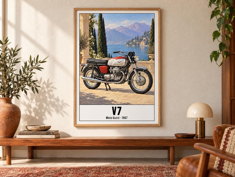 May include: A framed wall art print featuring a vintage Moto Guzzi V7 motorcycle parked on a stone terrace overlooking a lake and mountains. The text V7 and Moto Guzzi 1967 is printed in black at the bottom of the white border of the poster.