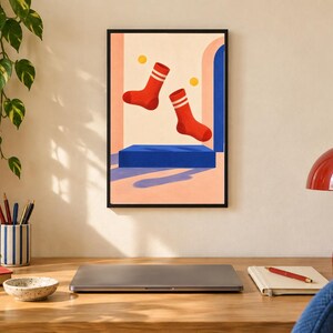 May include: A framed wall art print featuring a graphic illustration of two red socks with white stripes floating above a solid blue rectangular platform. The background consists of a light peach wall with a blue archway and two small yellow circles.
