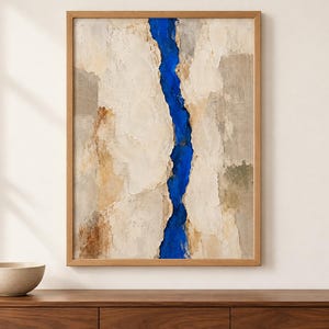 May include: A framed vertical wall art piece featuring a textured, layered composition in shades of beige, cream, and tan, bisected by a vibrant, deep blue vertical channel that runs from the top to the bottom edge of the canvas.