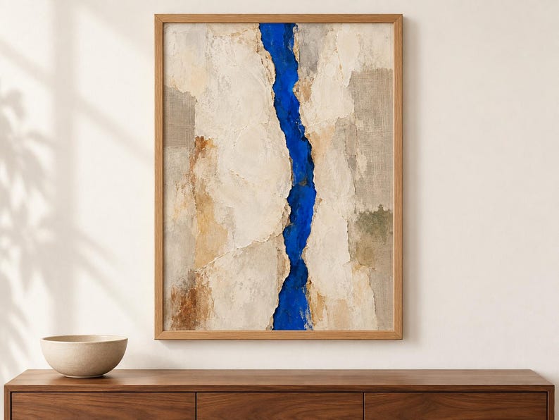 May include: A framed vertical wall art piece featuring a textured, layered composition in shades of beige, cream, and tan, bisected by a vibrant, deep blue vertical channel that runs from the top to the bottom edge of the canvas.