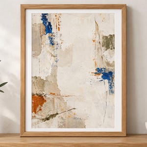 K&ouml;nnte beinhalten: Ein gerahmter abstrakter Wandkunstdruck mit einer texturierten, geschichteten Komposition in Off-White-, Creme- und Beiget&ouml;nen, akzentuiert durch kr&auml;ftige Striche in Tiefblau, gebranntem Orange und ged&auml;mpftem Olivgr&uuml;n, in einem hellen Holzrahmen.