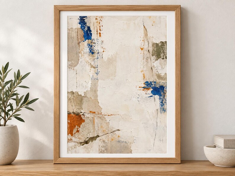 K&ouml;nnte beinhalten: Ein gerahmter abstrakter Wandkunstdruck mit einer texturierten, geschichteten Komposition in Off-White-, Creme- und Beiget&ouml;nen, akzentuiert durch kr&auml;ftige Striche in Tiefblau, gebranntem Orange und ged&auml;mpftem Olivgr&uuml;n, in einem hellen Holzrahmen.