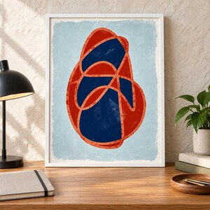 May include: A framed wall art print featuring an abstract design with a large, irregular, rounded shape in deep navy blue, overlaid with a continuous, textured, bright orange line that loops and curves across the entire central form.