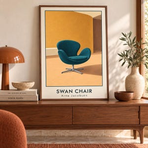 May include: A framed vertical art print featuring a teal-colored Swan chair with a metal base set against a warm yellow and orange background. The text SWAN CHAIR and Arne Jacobsen is printed in black at the bottom of the illustration within the frame.