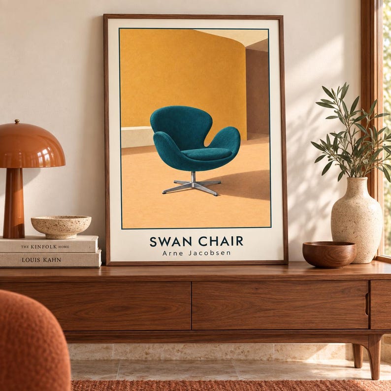 May include: A framed vertical art print featuring a teal-colored Swan chair with a metal base set against a warm yellow and orange background. The text SWAN CHAIR and Arne Jacobsen is printed in black at the bottom of the illustration within the frame.