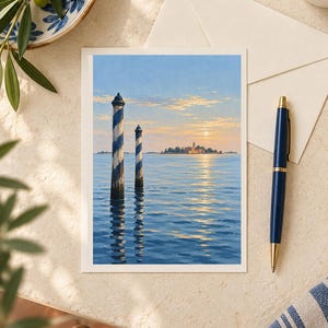 May include: A rectangular greeting card featuring a painting of two blue and white striped wooden mooring poles rising from calm water, with a distant island and a soft sunset sky in the background, displayed alongside a pen and an envelope.