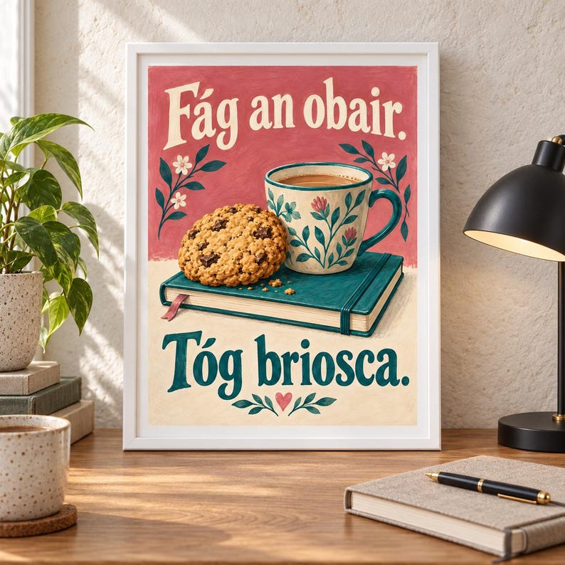 Pu&ograve; includere: Una stampa artistica incorniciata con sfondo rosso e il testo F&aacute;g an obair, e una sezione inferiore color crema con il testo T&oacute;g briosca. L'illustrazione mostra un biscotto con gocce di cioccolato su un libro verde acqua accanto a una tazza.