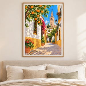 May include: A framed wall art print depicting a sunlit Mediterranean street scene with white and yellow buildings, vibrant orange trees, blooming pink bougainvillea, red potted flowers, and a tall stone bell tower under a clear blue sky.