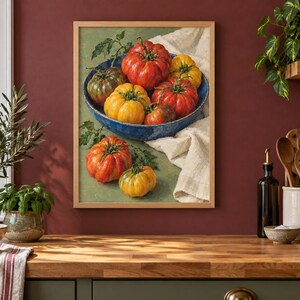 May include: A framed wall art print depicting a collection of heirloom tomatoes in a blue bowl and on a surface. The tomatoes are red, yellow, and green with visible stems and leaves. A white cloth is draped under the bowl, all set against a green background.