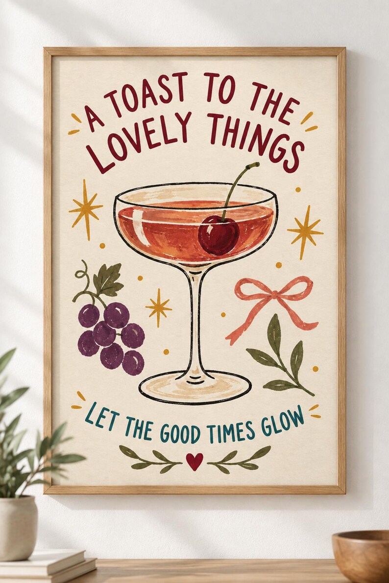 May include: A framed wall art print featuring a cocktail glass with a cherry, a cluster of purple grapes, a pink ribbon, and gold star accents. The text reads A TOAST TO THE LOVELY THINGS and LET THE GOOD TIMES GLOW, with a small red heart at the bottom.