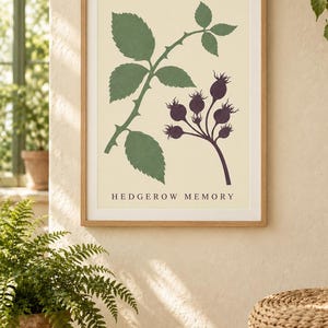 May include: A framed wall art print featuring a botanical illustration of a green rose leaf stem and a cluster of dark purple rose hips on a cream background, with the text HEDGEROW MEMORY printed in black at the bottom of the print.