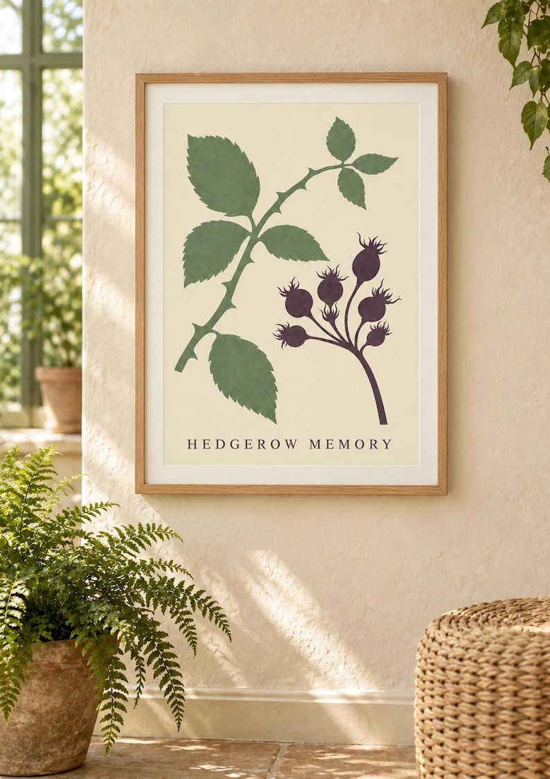May include: A framed wall art print featuring a botanical illustration of a green rose leaf stem and a cluster of dark purple rose hips on a cream background, with the text HEDGEROW MEMORY printed in black at the bottom of the print.