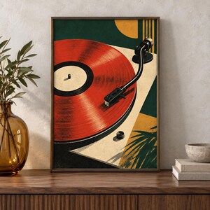 May include: A framed art print featuring a stylized illustration of a red vinyl record on a turntable. The composition includes geometric shapes in dark green, mustard yellow, and cream, with a black tonearm and a subtle palm leaf silhouette.