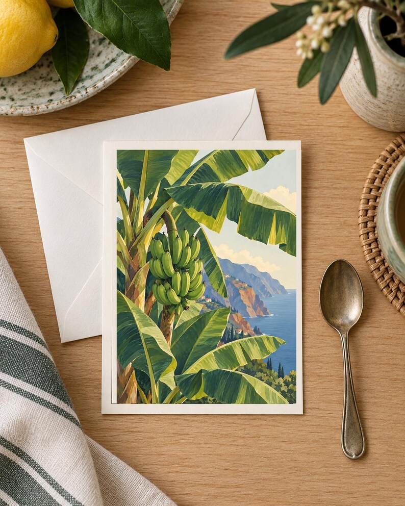 May include: A rectangular greeting card featuring a vibrant illustration of a banana tree with a large bunch of green bananas in the foreground, set against a scenic coastal landscape with blue ocean waters and cliffs under a clear sky.