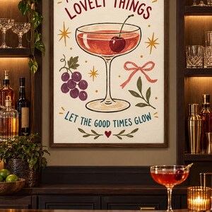 May include: A framed wall art print featuring a cocktail glass with a cherry, a cluster of purple grapes, a pink ribbon, and green leaves. The text reads A TOAST TO THE LOVELY THINGS and LET THE GOOD TIMES GLOW in red and teal lettering on a cream background.