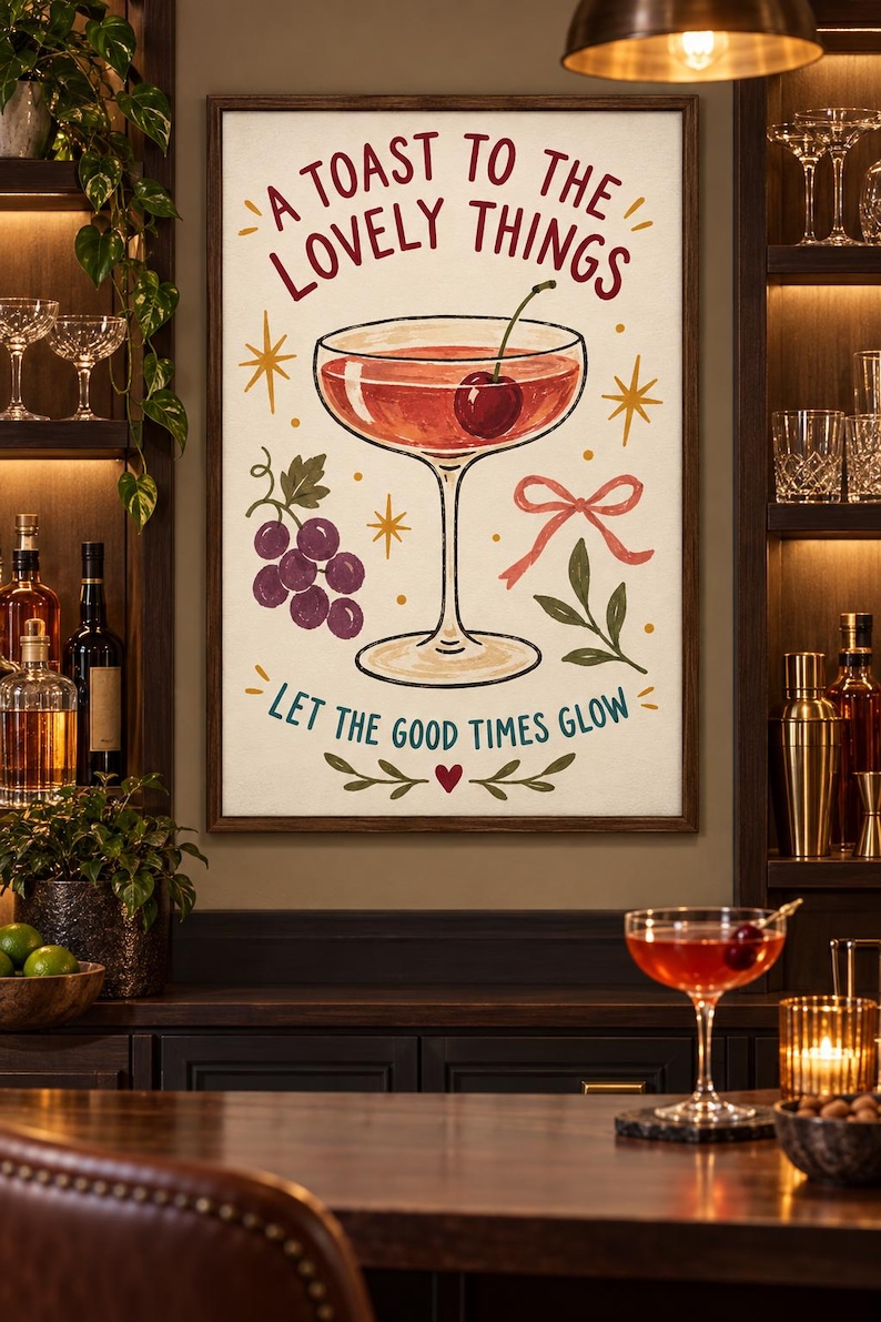 May include: A framed wall art print featuring a cocktail glass with a cherry, a cluster of purple grapes, a pink ribbon, and green leaves. The text reads A TOAST TO THE LOVELY THINGS and LET THE GOOD TIMES GLOW in red and teal lettering on a cream background.