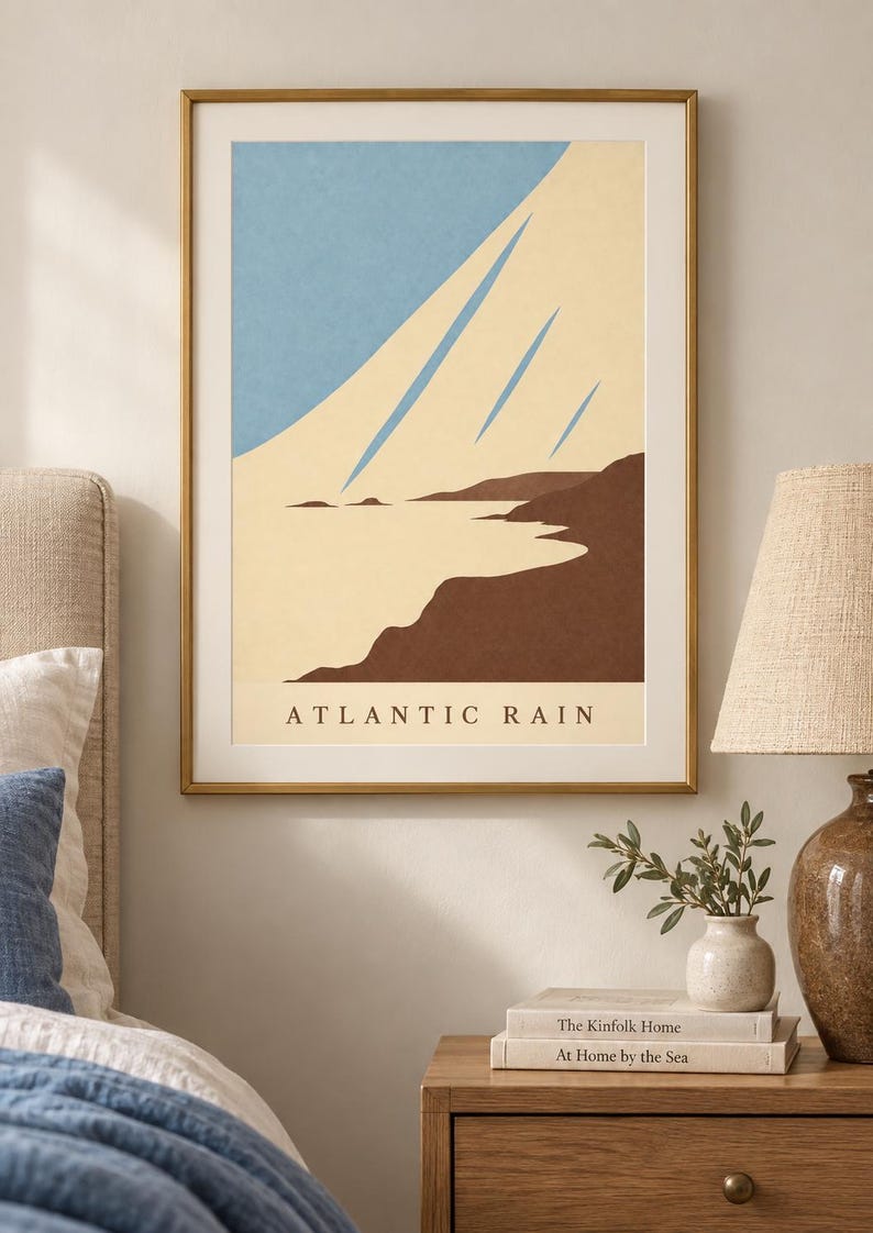 May include: A framed wall art print titled ATLANTIC RAIN featuring a minimalist landscape illustration with a light blue sky, cream-colored clouds, and dark brown coastal cliffs. The artwork is enclosed in a thin gold-toned metal frame.