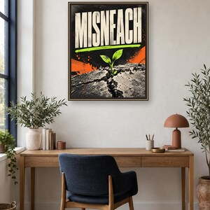 May include: A rectangular framed wall art piece featuring the word MISNEACH in large white capital letters. Below the text, a bright green sprout emerges from a cracked, dark gray textured surface, accented by vibrant orange graphic splashes.