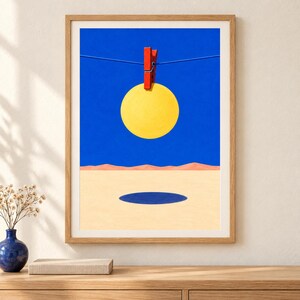 Peut inclure: Une impression d'art encadr&eacute;e repr&eacute;sentant un paysage surr&eacute;aliste avec un cercle jaune vif suspendu par une pince &agrave; linge rouge sur une fine ligne bleue contre un ciel bleu profond, au-dessus d'un sol d&eacute;sertique beige avec une ombre ovale bleue.