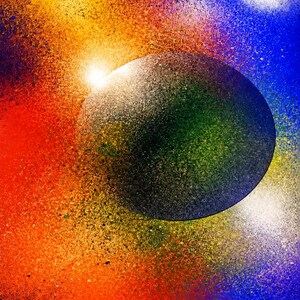 Op de afbeelding: Een cirkelvormig donkergrijs object met een getextureerd oppervlak is gecentreerd tegen een levendige achtergrond van spuitverfkleuren. Het omliggende veld vertoont een gradi&euml;ntovergang van felrood en oranje naar gele, blauwe en paarse spikkels.