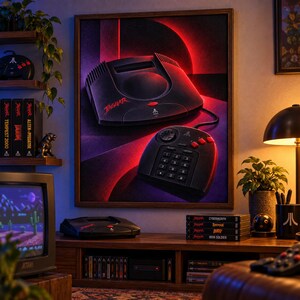 K&ouml;nnte beinhalten: Ein gerahmter Wandkunstdruck, der eine schwarze Atari Jaguar Videospielkonsole und den dazugeh&ouml;rigen Controller vor einem dunklen Hintergrund mit roter Neonbeleuchtung zeigt. Die Konsole tr&auml;gt den Schriftzug Jaguar in roter Farbe.